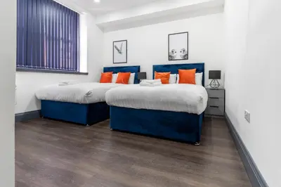 two beds in a white room with orange pillows at New Zealand House Apartments by Happy Days in Liverpool