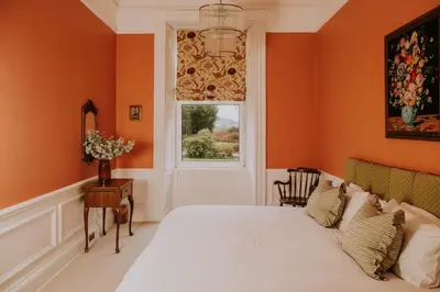 a bedroom with orange walls and a bed and a window at The Pheasant Lodge Spacious Georgian Apartment with Log Fire and Garden Views in Grange Over Sands
