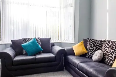 a living room with a leather couch with colorful pillows at Modern 5 Bed Near LFC Stadium in Liverpool