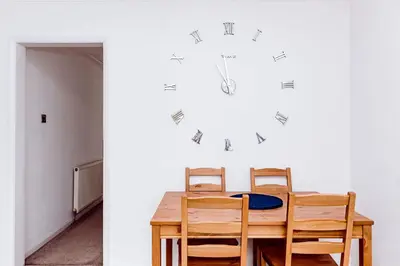 a dining room table with chairs and a clock on the wall at Willow Chalet near Cartmel & Lake Windermere in Flookburgh