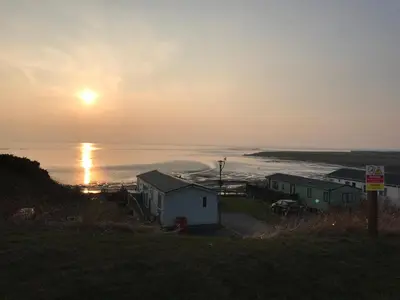 a sunset over the ocean with houses on a hill at Bobby's Bolthole in Heysham