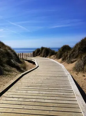 a wooden boardwalk leading to the ocean on a beach at Dora Cottage in Formby