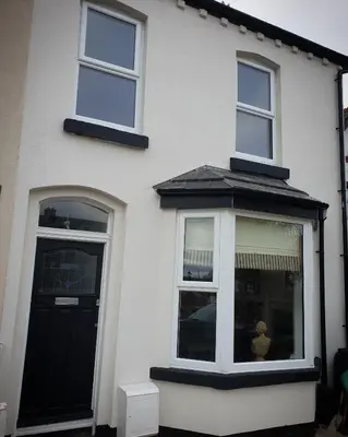 a white house with a black door and windows at Dora Cottage in Formby
