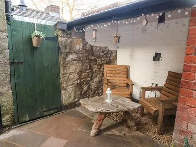 a patio with a table and a bench and a green door at Myrtle Cottage in Preston