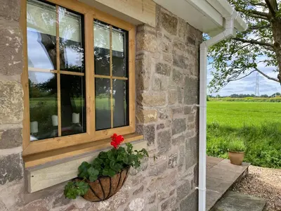 a window on a stone house with a red flower at Cosy Alpine Cottage in the heart of Lancashire in Catterall