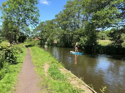 a woman is standing on a paddle board in a river at Cosy Alpine Cottage in the heart of Lancashire in Catterall