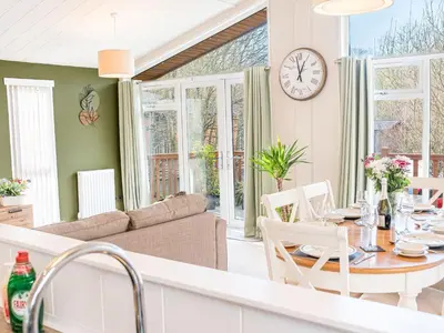 a kitchen and living room with a table and a clock at Fern Lodge in Grange Over Sands
