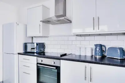 a kitchen with white cabinets and a black counter top at Cosy 3 bedroom house near Anfield Stadium in Liverpool