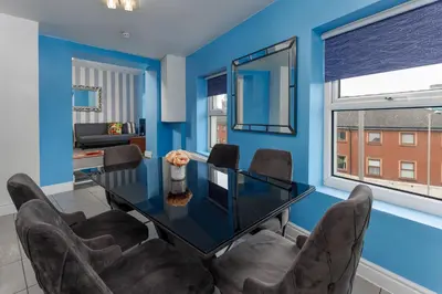 a dining room with blue walls and a glass table and chairs at Snuggle Cove Apartments By Bella Vita Stays in Liverpool