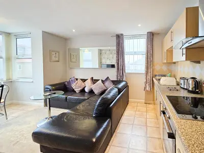 a living room with a leather couch and a kitchen at Sunrise Suite in Blackpool