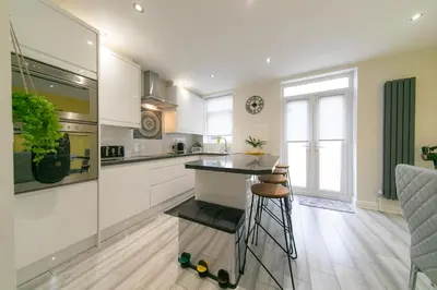 a kitchen with white cabinets and a counter with stools at Stunning house near Blackpool attractions in Blackpool