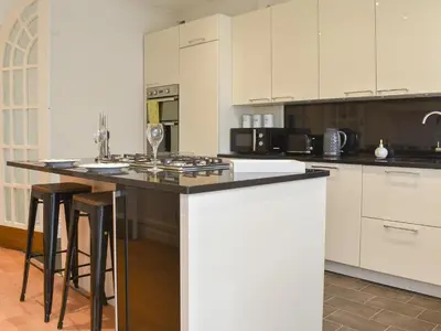 a kitchen with white cabinets and a island with bar stools at Honeybee Cottage in Lytham St Annes