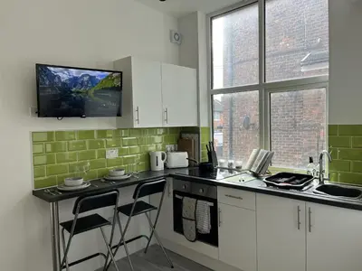 a kitchen with white cabinets and a tv on the wall at Modern 1 bed studios for comfy stay in Preston in Preston