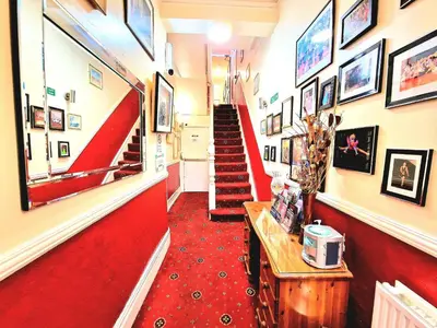 a red carpeted hallway with red stairs and pictures on the walls at Sleep Well Hotel in Blackpool