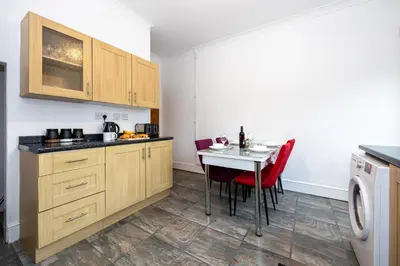 a kitchen with wooden cabinets and a table with red chairs at Cosy Two bedroom Terrace Blackburn in Cherry Tree