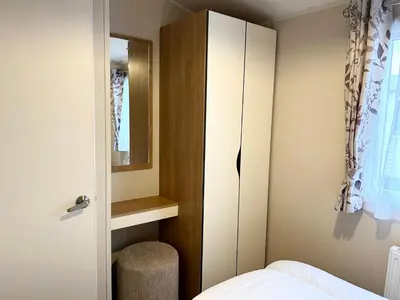 a bedroom with a bed and a mirror and a cabinet at The SandyBel Caravan in Cark