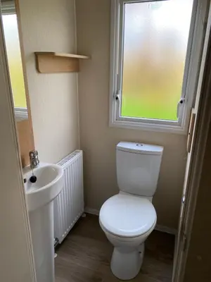 a bathroom with a white toilet and a sink at The SandyBel Caravan in Cark