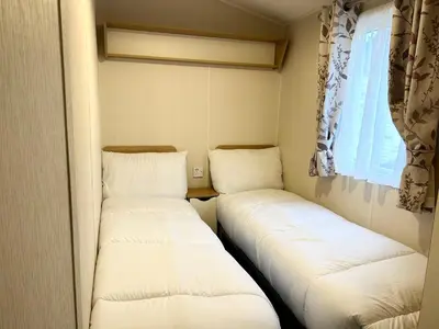 two beds in a small room with a window at The SandyBel Caravan in Cark