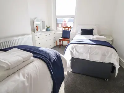 a white bedroom with two beds and a chair at Anandom in Blackpool