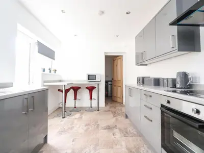 a kitchen with white cabinets and red stools at Anandom in Blackpool
