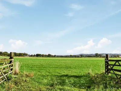 a fence in a field with green grass at Priory Barn in Burscough