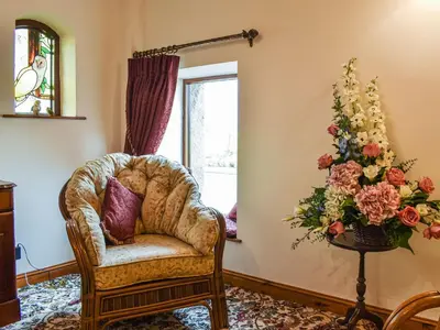 a room with a chair and a vase of flowers at Priory Barn in Burscough