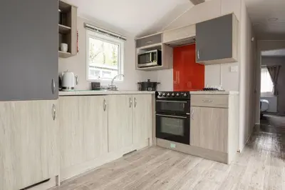 a kitchen with wooden cabinets and a stove top oven at Borwick Lakes Holiday Caravan (Partial Lake View) in Borwick