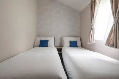 two twin beds in a small room with a window at Borwick Lakes Holiday Caravan (Partial Lake View) in Borwick