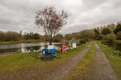 a dirt road next to a river with chairs on it at Borwick Lakes Holiday Caravan (Partial Lake View) in Borwick