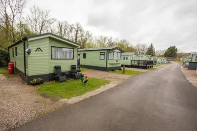 a row of green mobile homes on the side of a road at Borwick Lakes Holiday Caravan (Partial Lake View) in Borwick