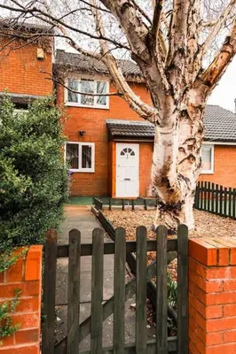 a fence in front of a house with a tree at Elegant 2 bed with hot tub and a host of amenities in Liverpool