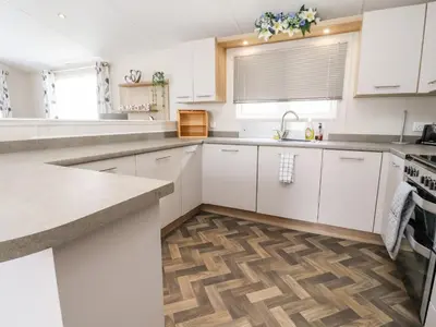a kitchen with white cabinets and a wooden floor at Rosella 38 in Morecambe