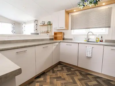 a kitchen with white cabinets and a wooden floor at Rosella 38 in Morecambe