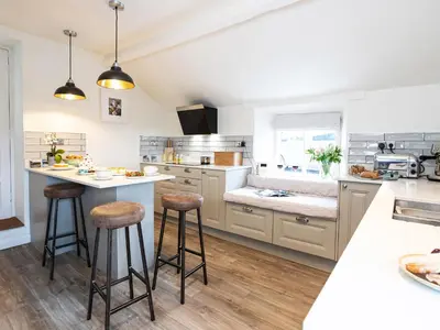 a kitchen with white counters and bar stools at Longlands Farm Cottage in Grange Over Sands