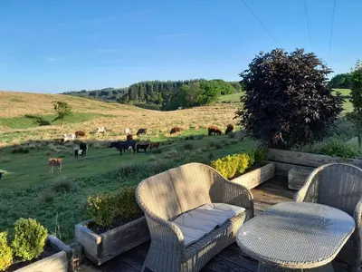 two chairs and a table on a deck with a field of cows at Cadshaw Country Views in Darwen