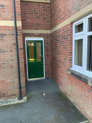 a green door on the side of a brick building at Kensington Luxury Apartment on Gated Development in Leafy edge of Chorley Town Centre in Chorley