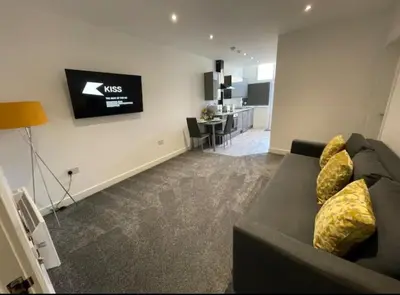 a living room with a black couch and a kitchen at Newly Refurbished Clarendon Apartments, Free WIFI, Parking in Blackpool