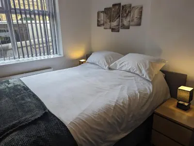 a bedroom with a bed with white sheets and a window at Station Apartments in Ashton in Makerfield