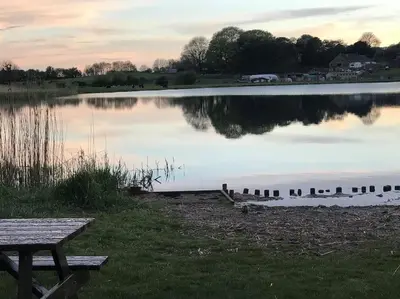 a bench sitting next to a lake at sunset at Modern 3 Bed Barn Conversion in Great Urswick in Great Urswick