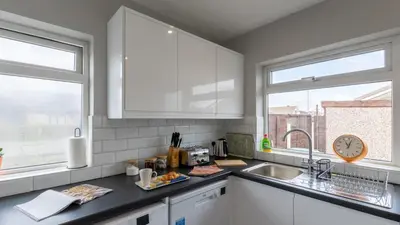 a kitchen with white cabinets and a sink and two windows at Altham Place-Free Parking Space in Morecambe