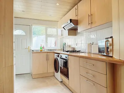 a kitchen with wooden cabinets and a washer and dryer at Bee Stays - Cooper House in Haydock