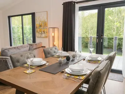 a dining room table with chairs and a wooden table with glasses at Watch Tree Lodge in Grange Over Sands