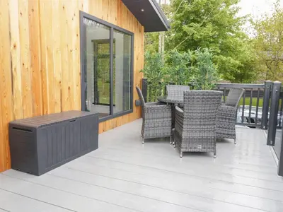 a patio with wicker chairs and a table on a deck at Watch Tree Lodge in Grange Over Sands