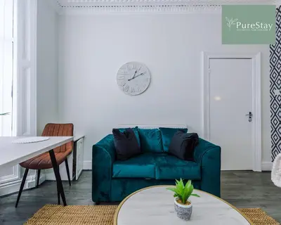 a living room with a green couch and a clock on the wall at Perfect Contractor House in Liverpool with 7 Beds By PureStay - 14 nights min! in Liverpool