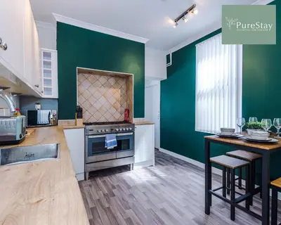 a kitchen with green walls and a stove and a table at Perfect Contractor House in Liverpool with 7 Beds By PureStay - 14 nights min! in Liverpool