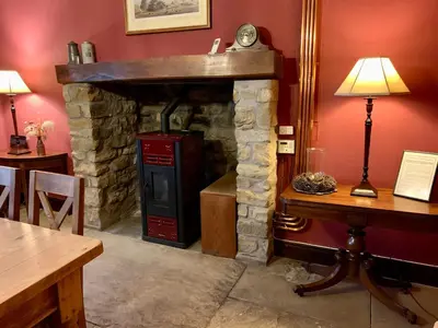 a stone fireplace in a room with a table and a lamp at Large Country Farmhouse in Waddington
