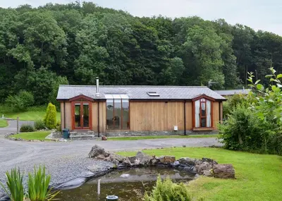a wooden cabin with a pond in front of it at Blenkett Wood Lodge Park in Kents Bank