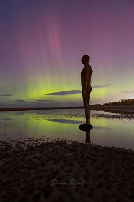 a statue standing on the beach under the northern lights at Lovely 2 Bed Full House By The Beach in Liverpool
