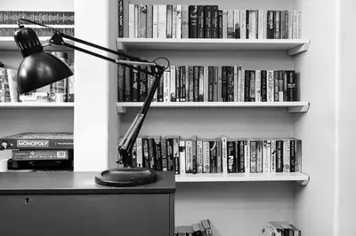 a desk with a lamp and a book shelf with dvds at The Riverside Tailor's Retreat at Wray in Wray